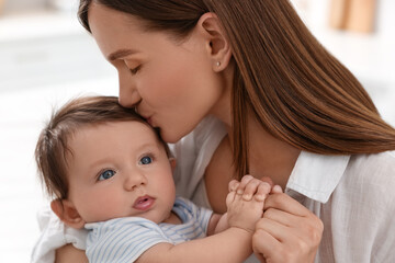 Happy mother kissing her little baby indoors, closeup
