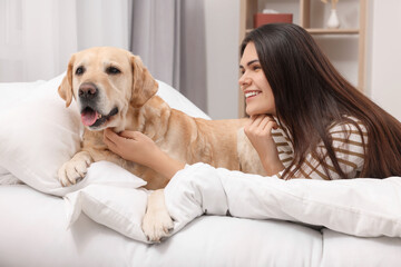 Happy woman with cute Labrador Retriever on bed at home