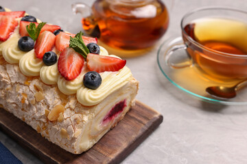 Tasty meringue roll with jam, cream, strawberry, blueberry, mint and aromatic tea on light grey table, closeup
