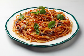 Delicious pasta with anchovies, tomato sauce and basil on white table