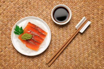 Sashimi set (raw salmon slices) served with funchosa, parsley, vasabi and soy sauce on wicker surface, flat lay