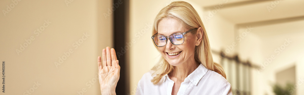 Wall mural pleased attractive mature businesswoman waving at webcam, having online call using laptop while sitt