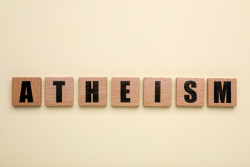 Word Atheism made of wooden squares with letters on beige background, top view