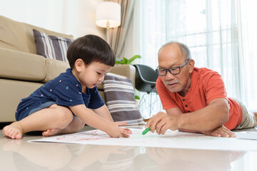 Asian Grandfather and Grandson drawing and coloring with Crayons together. Senior man and little...