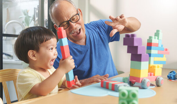 Joyful Asian Chinese child boy and his Grandfather playing game with building toy blocks at home together.