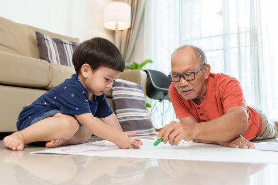 Asian Grandfather and Grandson drawing and coloring with Crayons together. Senior man and little child boy painting with Crayons on paper.