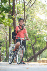 Fototapeta premium Happy Active Asian Chinese Senior man in helmet holding mobile phone or smartphone and taking selfie while travel with bicycle outdoors. Retirement activity, Relax, Exercise, wellness and lifestyle