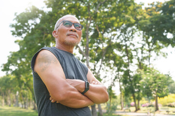 Naklejka na ściany i meble Portrait of Happy and healthy Asian Chinese senior man with arms crossed at park outdoor. Male smiling relaxing, exercising.