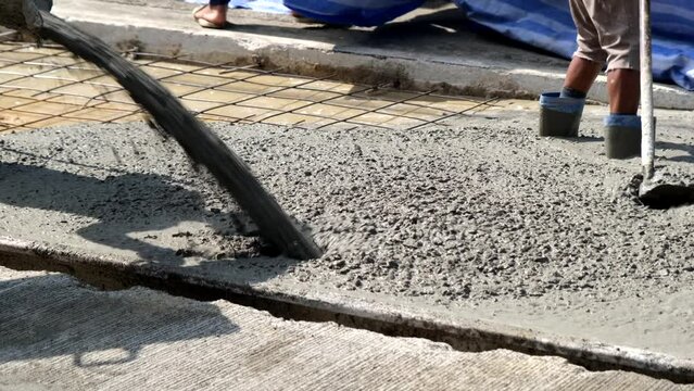 A construction worker is pouring mortar mixed with sand and stone to level the surface of a concrete road.