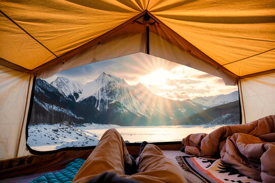 Traveler man relaxing inside a yellow tent with sunrise over Medicine Lake in winter at Jasper national park