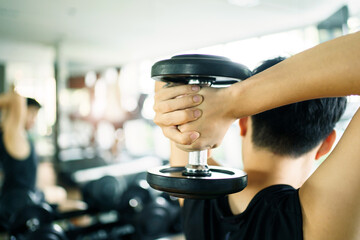 Active Asian sportsman doing a weight training exercise by lifting up a dumbbell, man lifting up or holding a heavy dumbbell in Overhead Tricep Extension position. Bodybuilding workout.