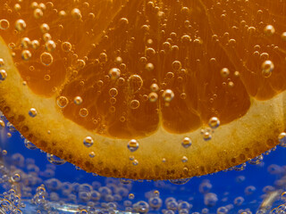 Slice of fresh orange slice in the water with bubbles, on  vibrant blue background