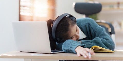 Online education, e-learning. Asian woman relaxing after studying using a laptop, listening to online lecture, taking notes, online study at home