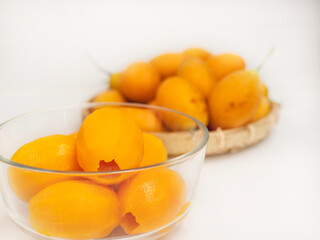 ripe juicy peeled marian plum or plum mango fruit serve in glass bowl and woven bamboo tray over...