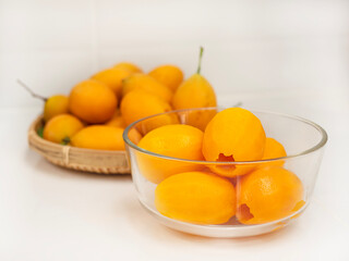 ripe juicy peeled marian plum or plum mango fruit serve in glass bowl and woven bamboo tray over white kitchen background, thailand fresh asian famous tropical fruit