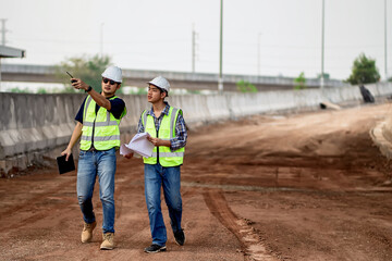 A team of civil engineers and architects wearing safety gear inspect the construction site of a high concrete bridge at a highway construction site.