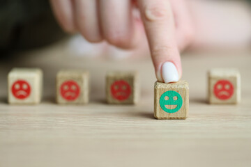 Finger of woman moves out wooden cube with positive emoji