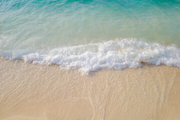 Fototapeta na wymiar White foam Wave Sea clear blue water against on sand beach on summer 