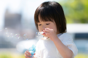 新緑の初夏の公園でシャボン玉をして遊ぶ小さな女の子