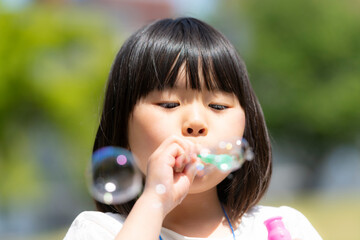 新緑の初夏の公園でシャボン玉をして遊ぶ女の子