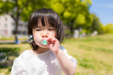 新緑の初夏の公園でシャボン玉をして遊ぶ小さな女の子
