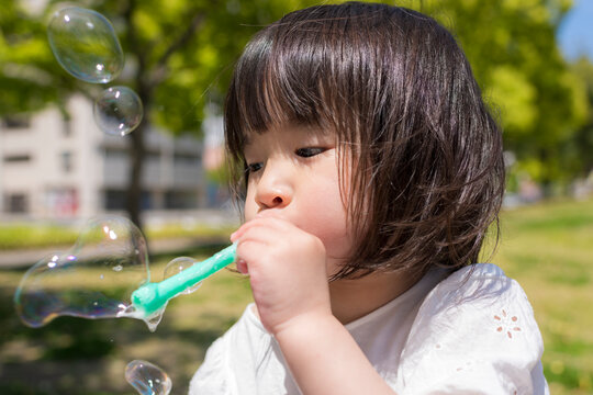 新緑の初夏の公園でシャボン玉をして遊ぶ小さな女の子