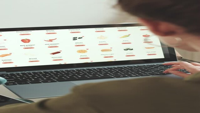 Vertical over the shoulder shot of woman scrolling through catalog while ordering food products online on laptop from home