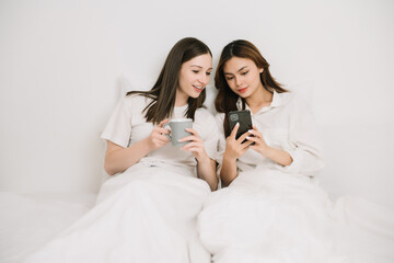 Attractive lesbian couple use mobile phone, tablet watch movie on bed. Beautiful sibling in pajamas...