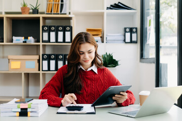 Young beautiful woman typing on tablet and laptop while sitting at the working wooden table office.