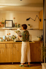 Beautiful woman makes a bouquet of flowers on kitchen at home, decorating her modern apartment with fresh flowers