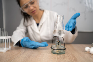 School chemistry classroom, teacher shows science experiment by setting spirit lamp with flask on...
