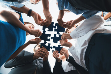 Below view of diverse corporate officer workers collaborate in office connecting puzzle pieces as...