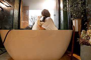 Fototapeta na wymiar Young woman hugs with her cute dog in bathtub during SPA procedures in bathroom. Concept of friendship with pets and care
