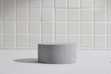 A cylinder podium in gray color isolated on white mosaic tiles background. Blank space on the podium for products or goods presentation