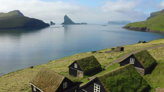 4k drone forward video (Ultra High Definition) of Bour village with typical turf-top houses and Tindholmur cliffs on background. Aerial morning view of Vagar island, Faroe, Denmark, Europe.