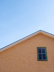 The facade and roof of an old yellow house against a white sky