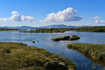 Beautiful scenery in Thingvellir National Park, Iceland, with a lake Thingvallavatn, mountain ridges and clouds in the blue sky. 