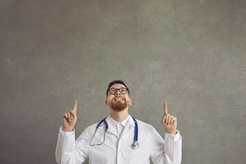 Smiling young male doctor showing index fingers up offering something to choose from. Man in...