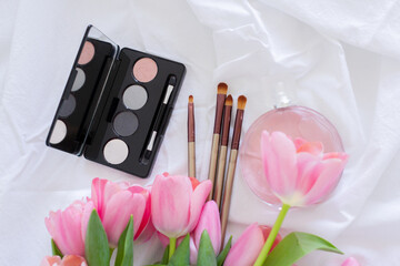 Obraz na płótnie Canvas Pink tulips, eye shadow palette, brushes and perfume bottle on white background, women makeup cosmetics set
