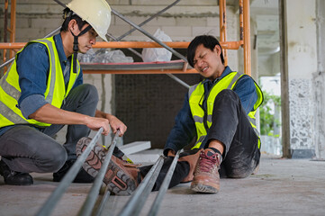 Young Asian builder falls from a height at a construction site. An engineer supervising the construction came to the aid of a construction worker who fell from a height with knee and leg injuries.