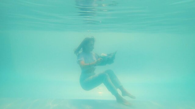 girl reading a newspaper sitting at the bottom of the pool
