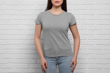 Woman wearing stylish gray T-shirt near white brick wall, closeup