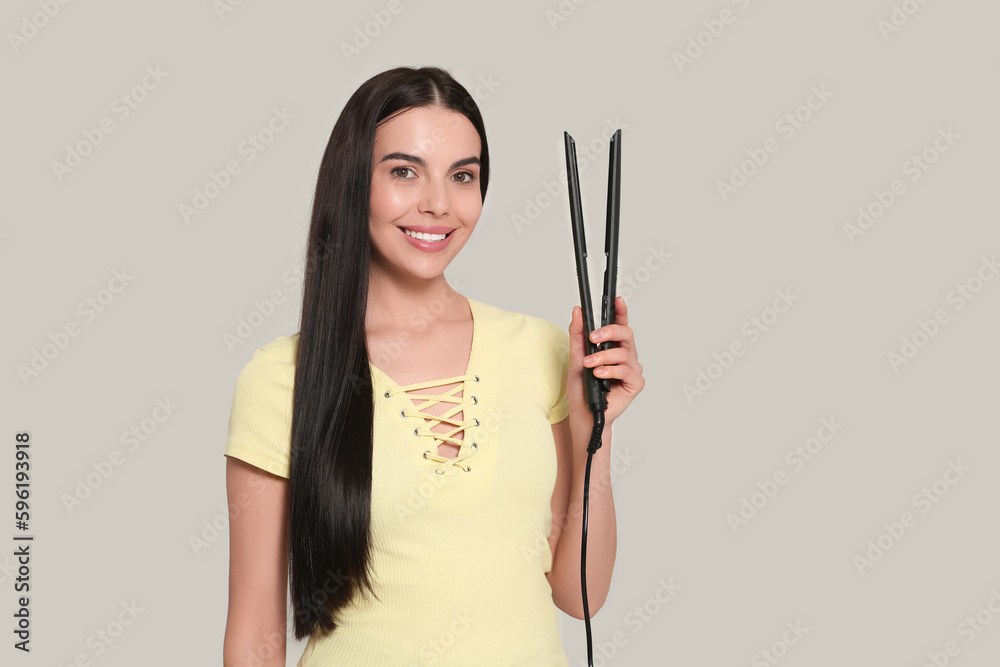 Canvas Prints Beautiful happy woman with hair iron on light grey background. Space for text