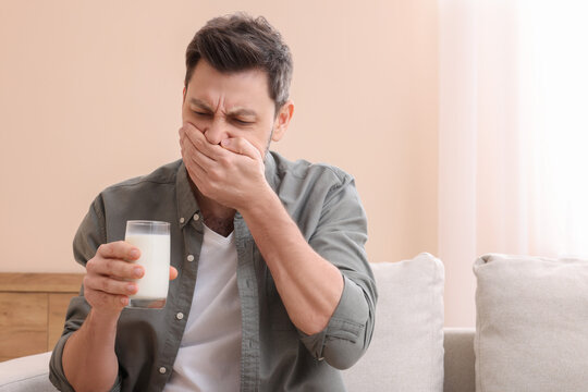 Man with glass of milk suffering from lactose intolerance at home, space for text