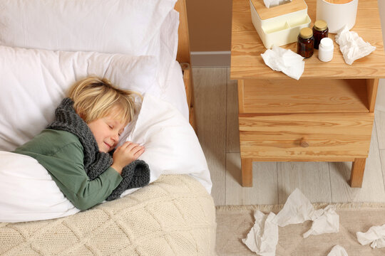 Sick boy lying in bed near bunch of napkins on floor at home, above view