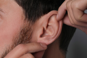 Fototapeta premium Man touching his ear on grey background, closeup