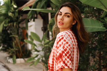 Outdoor fashion portrait of  brunette young woman posing near palm trees and wearing modern trendy...
