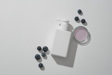 Top view of white blank plastic cosmetics container for cleanser or lotion with blueberries and essence on white background. Blueberry extract have anti-aging, healing, and skin-regenerating effects.