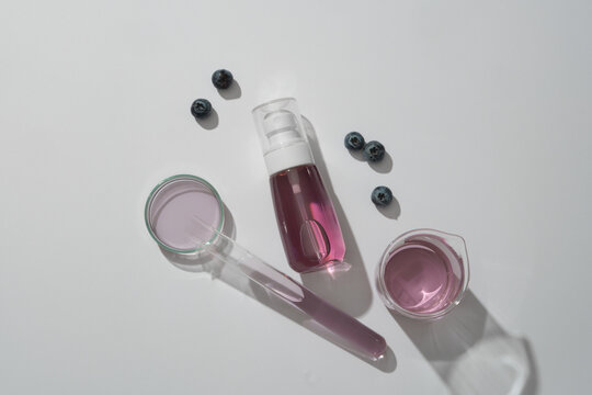 Blank spray bottle containing purple liquid, blueberries and essence on lab glassware decorated on white background. Mockup scene for advertising. Natural cosmetic concept