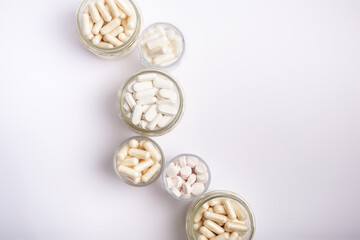 Organic food supplements, vitamins and minerals in glass jars from above on white background. 